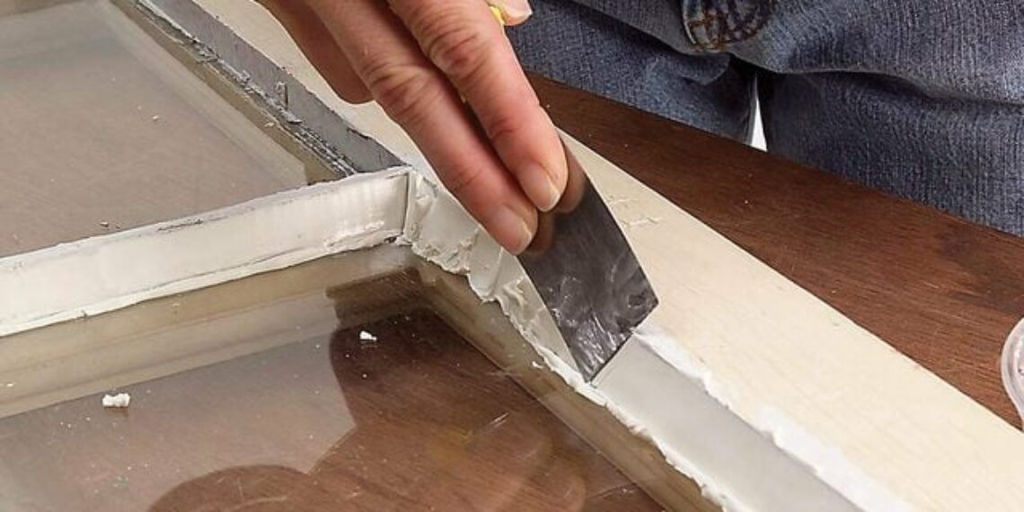 Wooden window frame with putty being smoothed in along the edge.