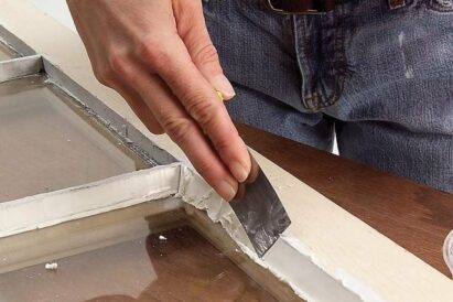 Wooden window frame with putty being smoothed in along the edge.