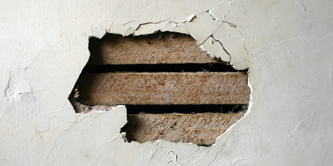 Hole in plaster wall exposing wooden lathe