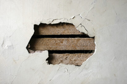 Hole in plaster wall exposing wooden lathe